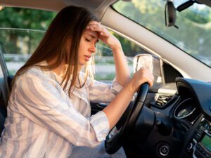 Mujer joven con dolor de cabeza o migrañas al volante producidas por la fatiga.